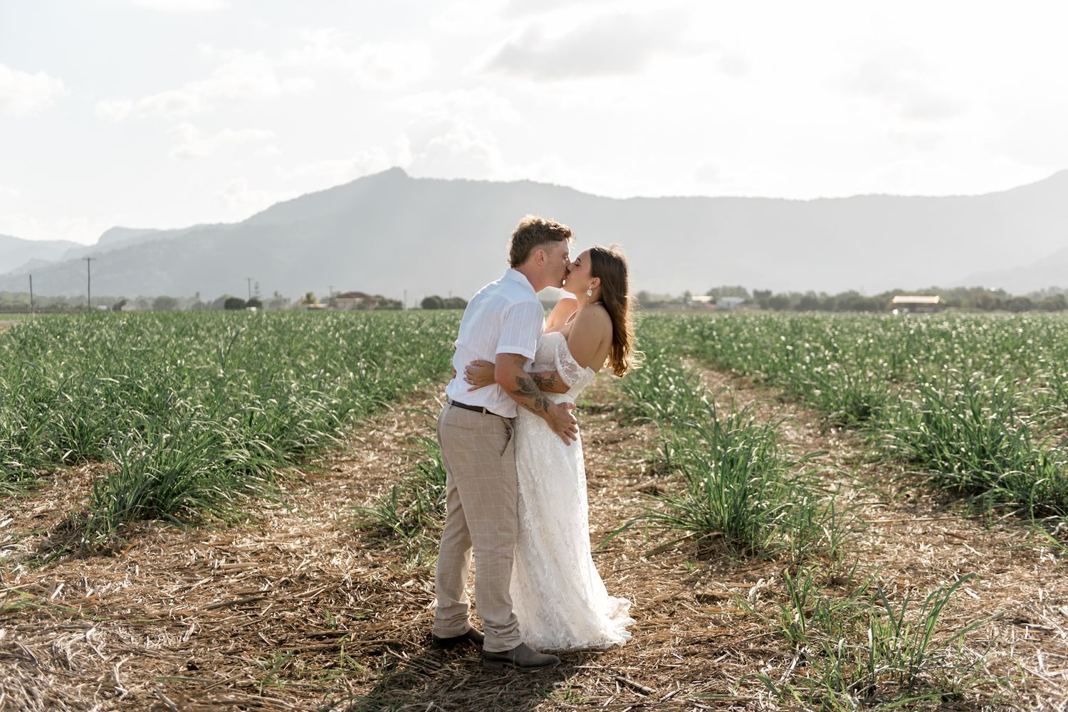 Wedding couple sharing a romantic kiss in a scenic green field with mountains behind them.