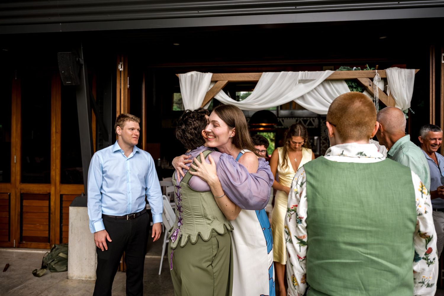Guests embrace and greet each other at an outdoor wedding celebration.