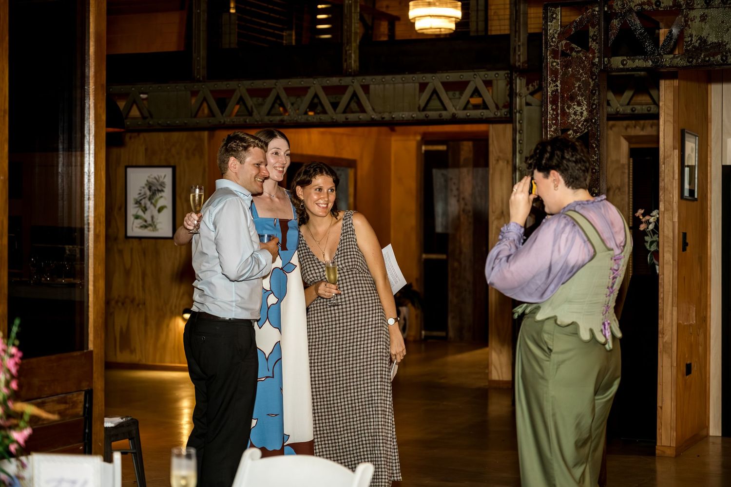 Wedding guests laughing as a photographer captures their photo inside a rustic venue.