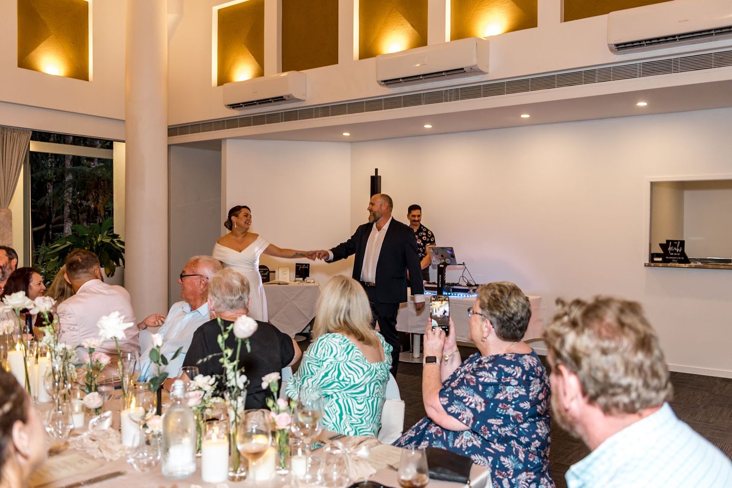 Bride and groom addressing guests during wedding reception speech in a warmly lit elegant venue.