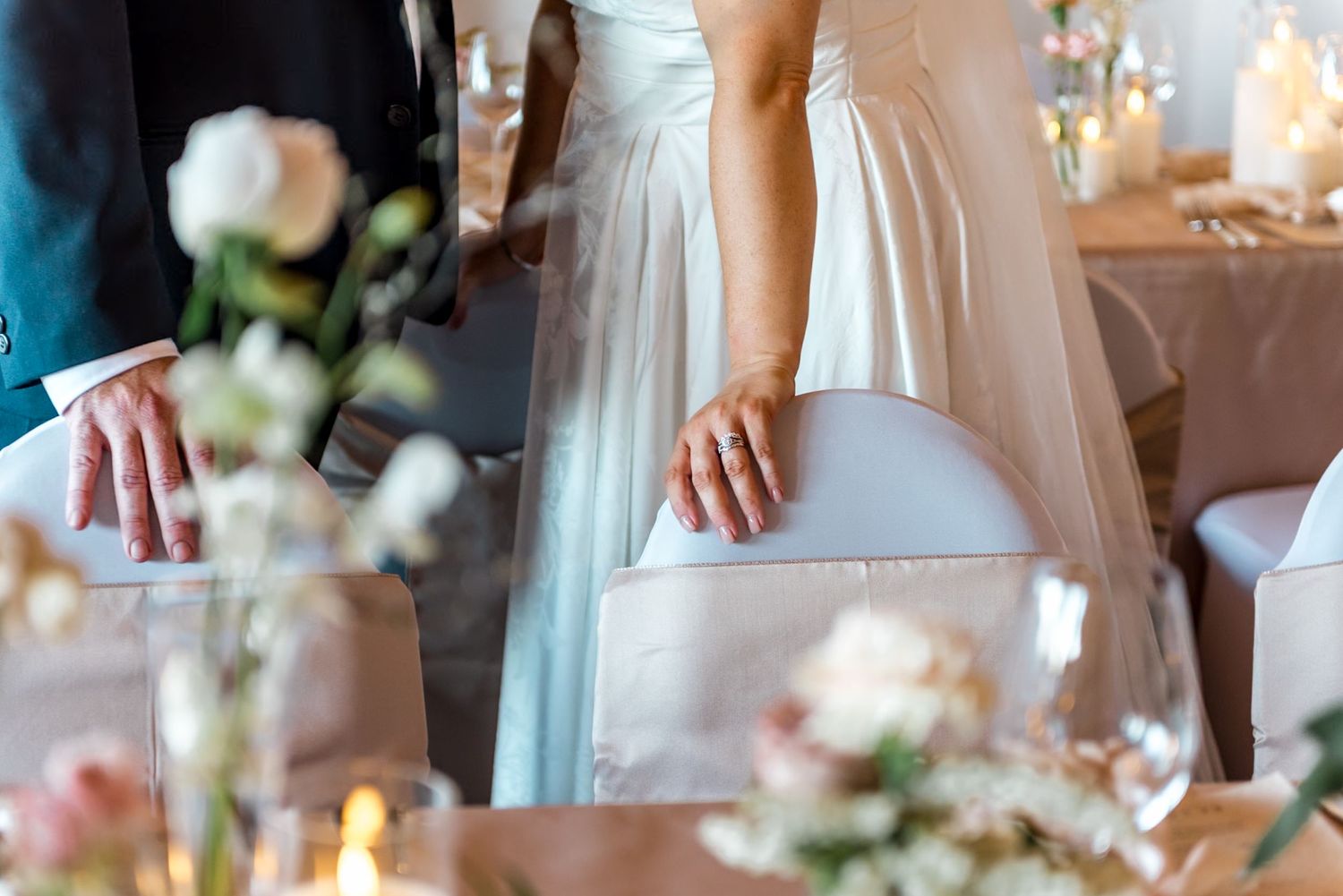 Bride and groom standing side by side with wedding rings visible against elegant reception table setting.