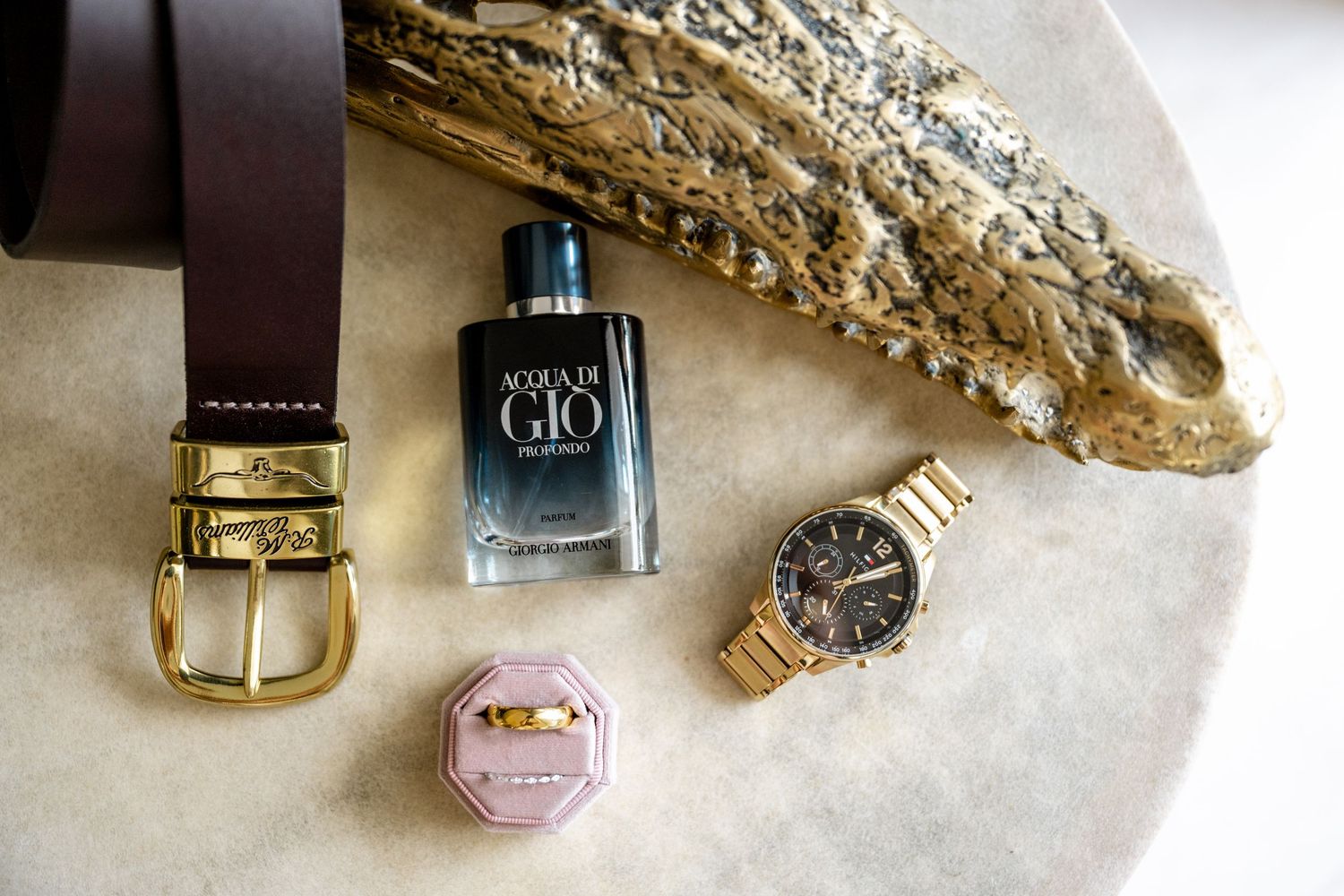Groom flat lay featuring Acqua di Gio cologne, leather belt, gold watch, and wedding ring box.