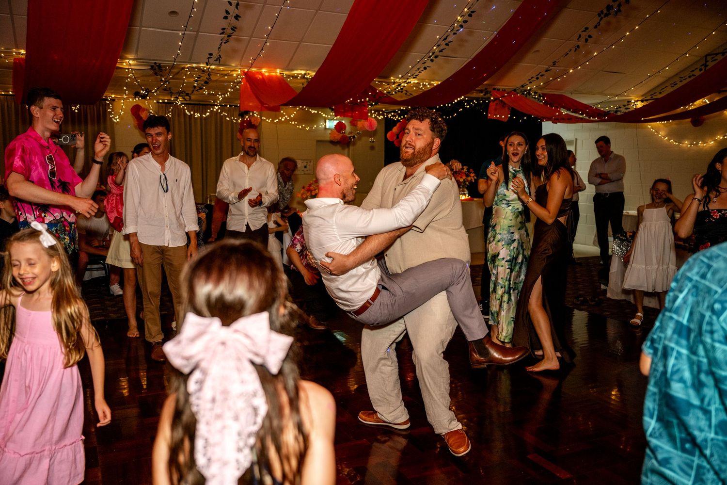 Groomsmen lifting each other playfully on the dance floor at a wedding.