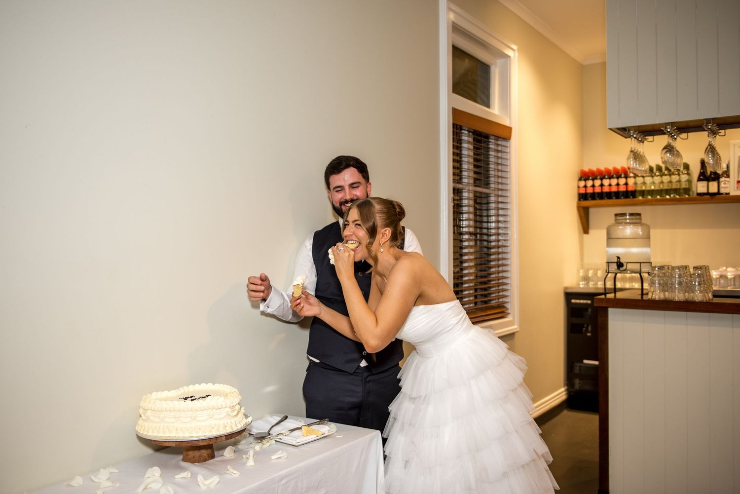 Newlyweds sharing a bite of wedding cake during their indoor reception celebration.