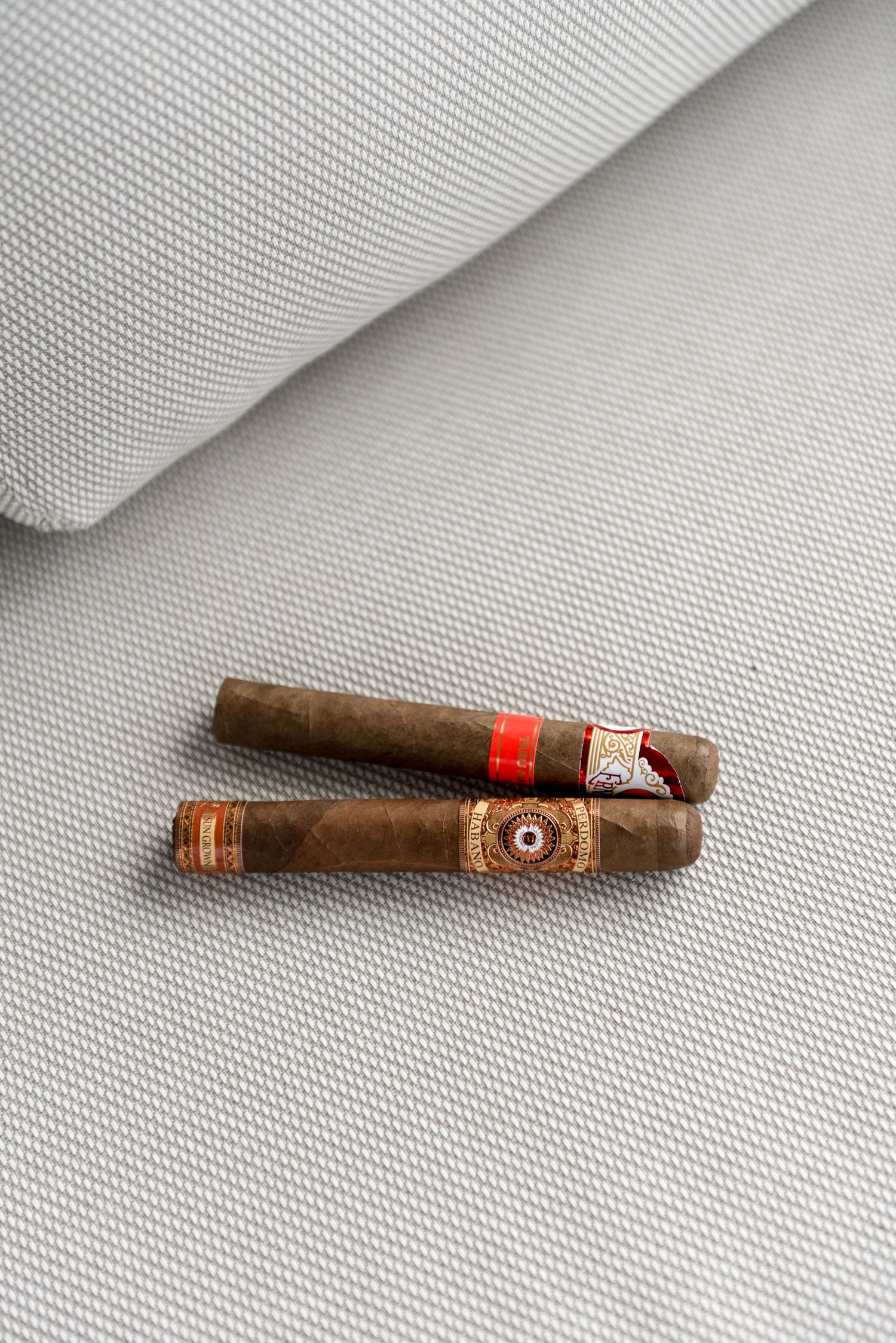 Two premium cigars with decorative bands resting on a grey fabric surface.