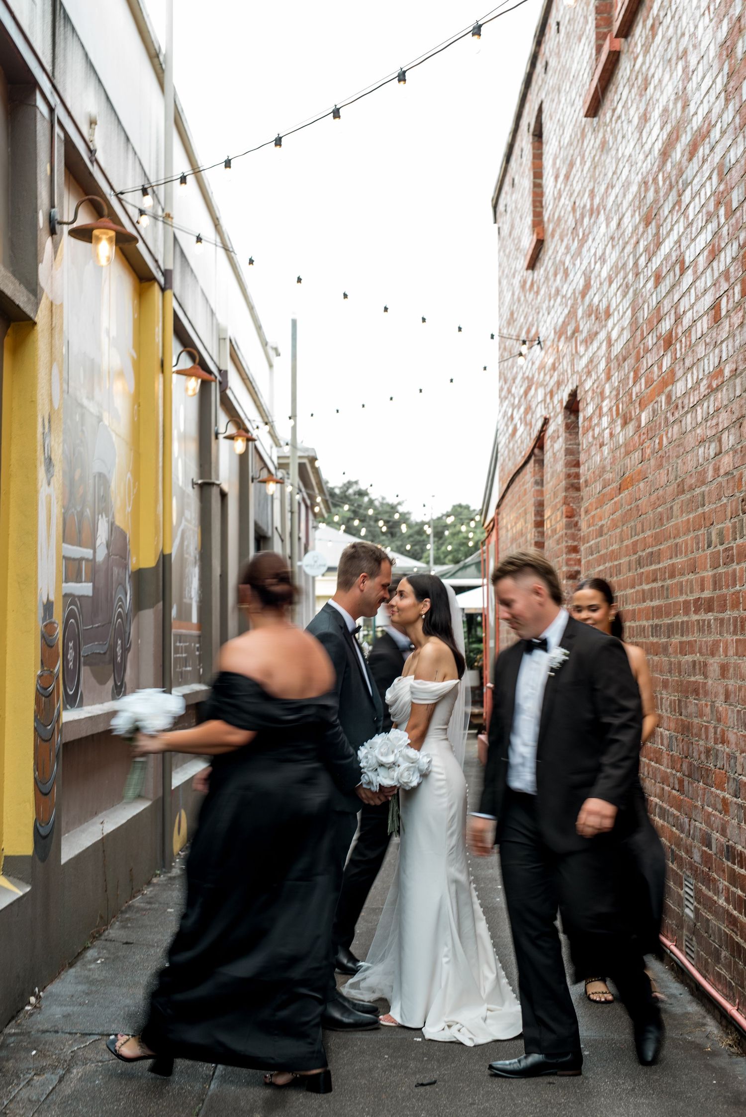 Bride and groom sharing a kiss in a festoon-lit urban laneway.