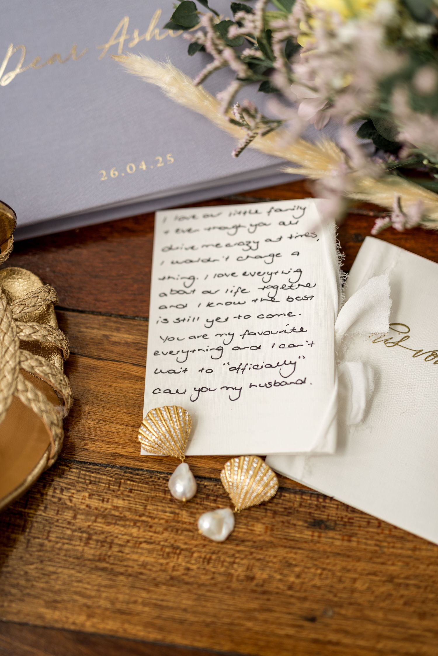 Close-up of handwritten wedding vows with gold shell pearl earrings on a wooden table.