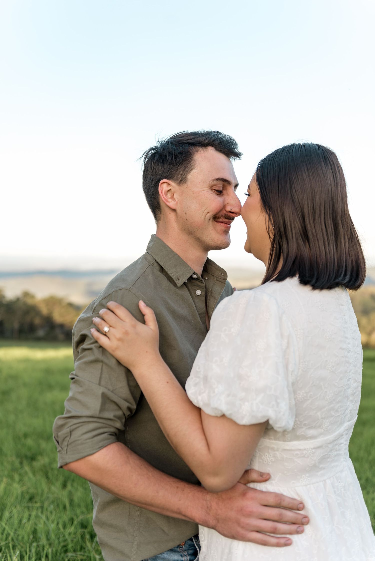 Couple sharing a tender nose-to-nose moment in a sunlit green field.