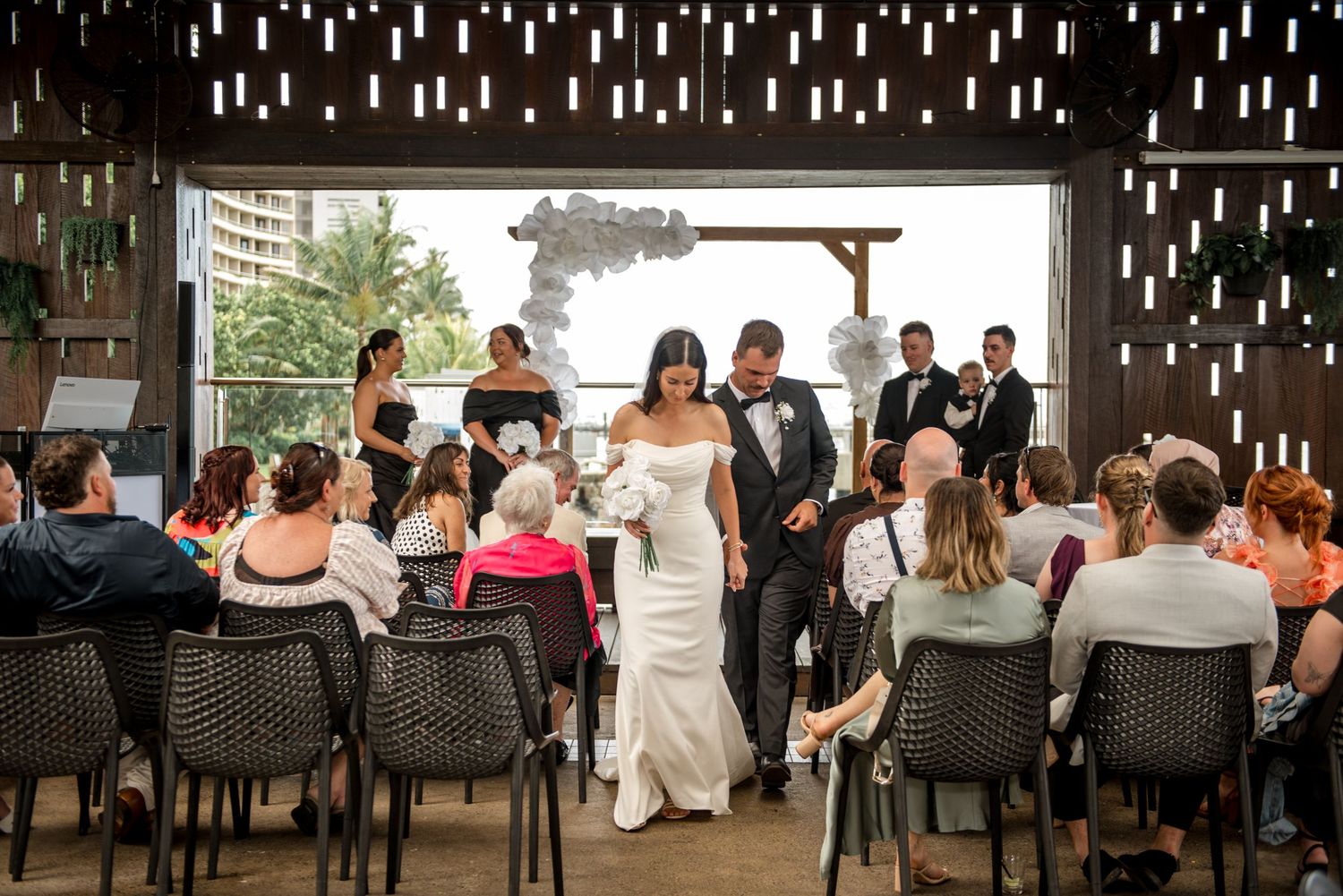 Bride and groom walking down aisle together after wedding ceremony in rustic open venue.