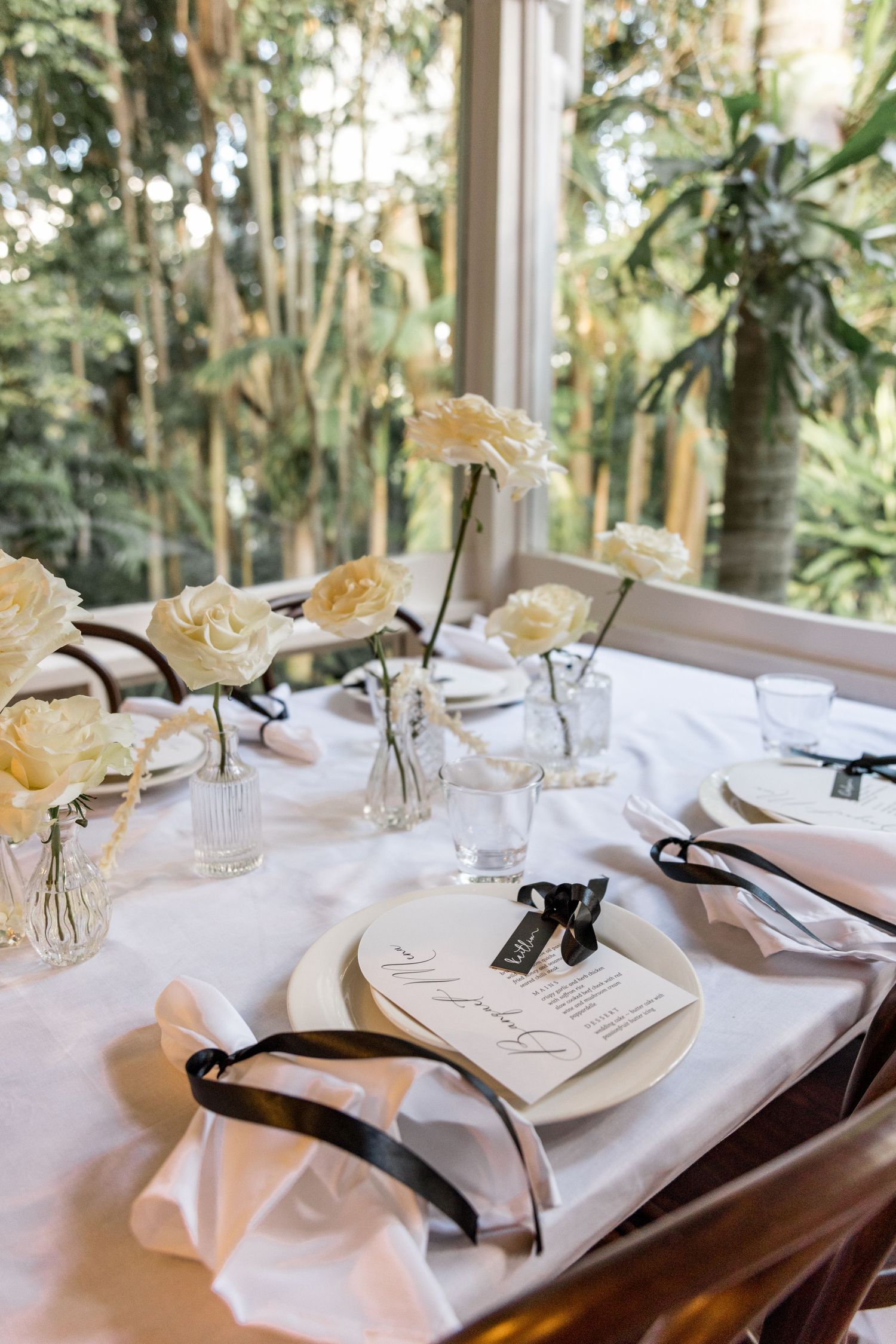 Elegant wedding table setting with white roses, black ribbon napkins, and menu cards.