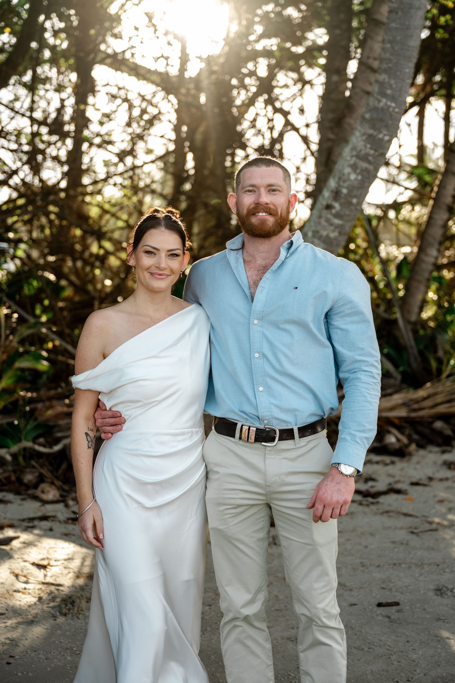 Smiling bride in white gown and groom in light blue shirt posing at beach wedding at Four Mile Beach, Port Douglas.