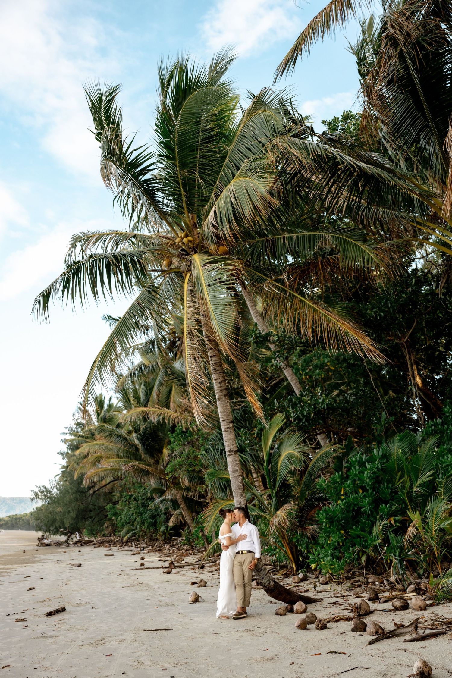 Bride and groom embrace under a leaning coconut palm tree on a scenic tropical beach at Four Mile Beach, Port Douglas.