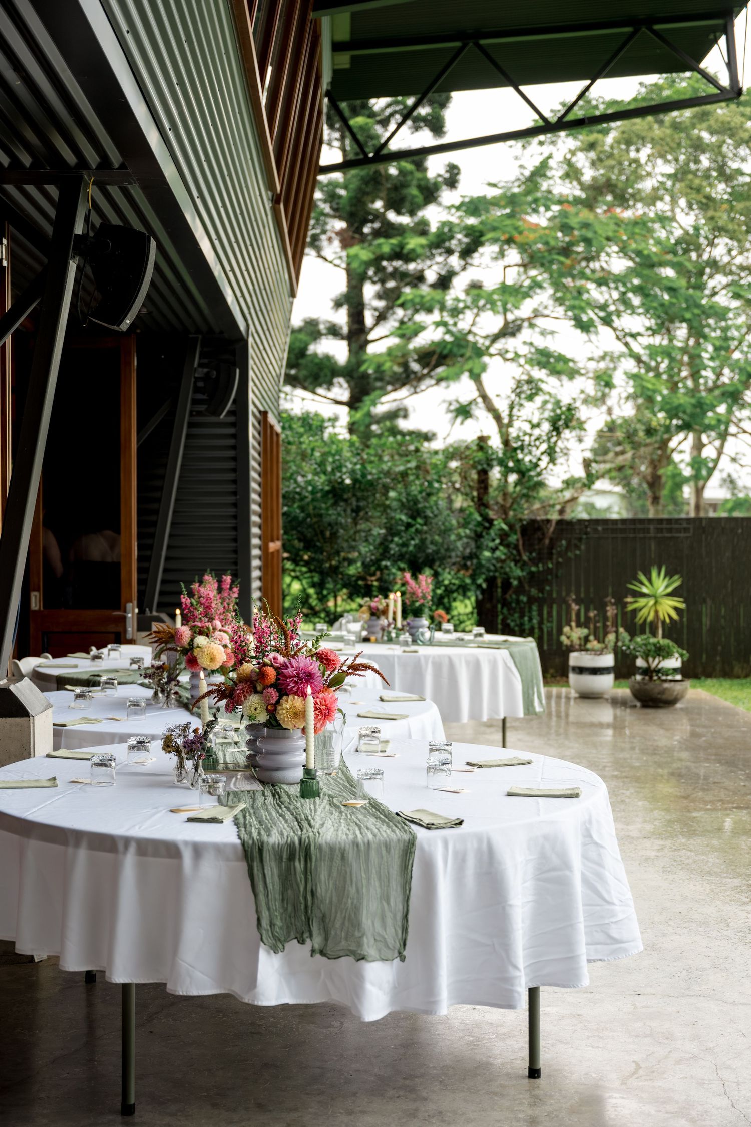 Elegant outdoor wedding reception table with white linen, green runner, and colorful floral centerpiece.