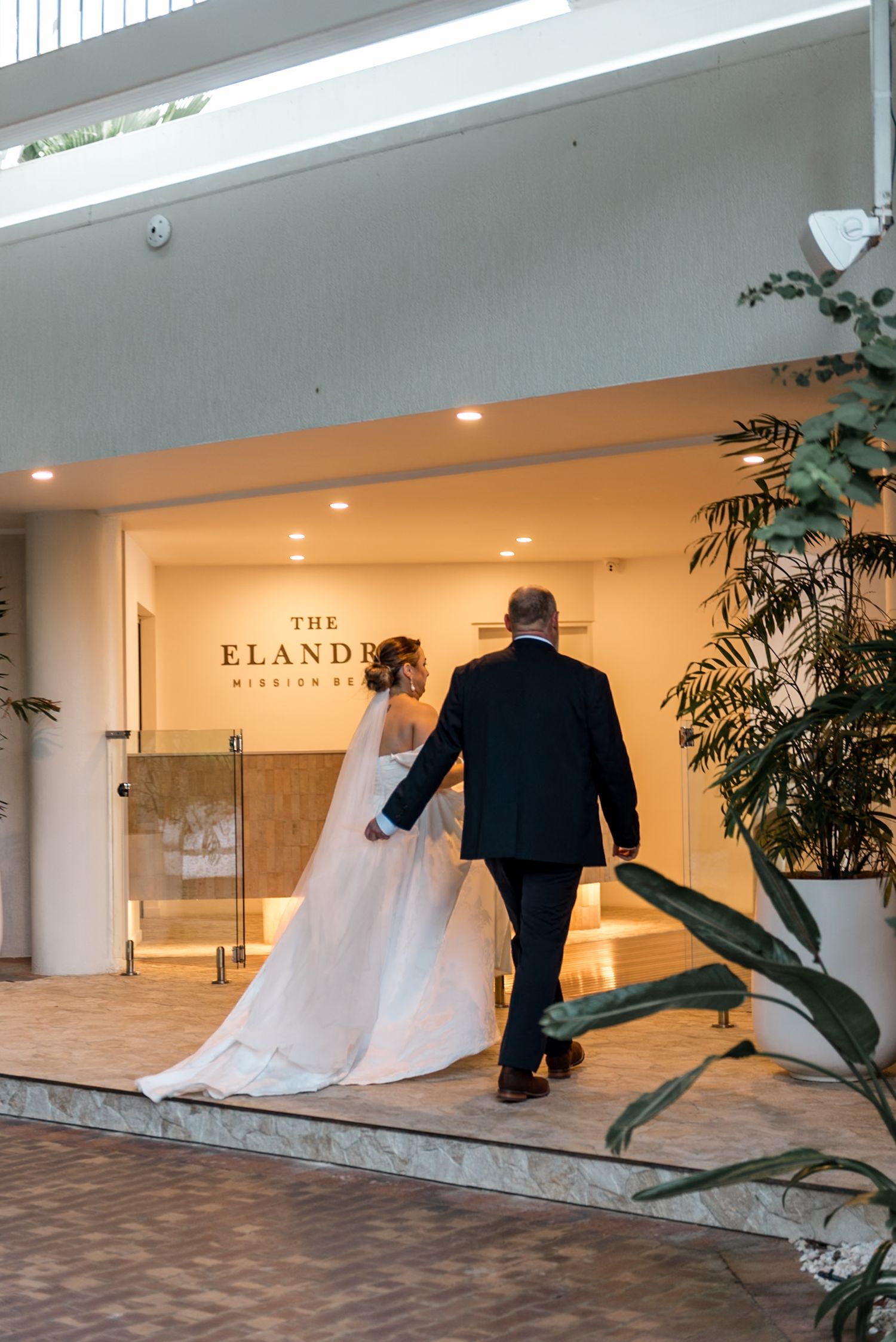 Bride and escort entering The Elandra Mission Beach wedding venue at dusk.