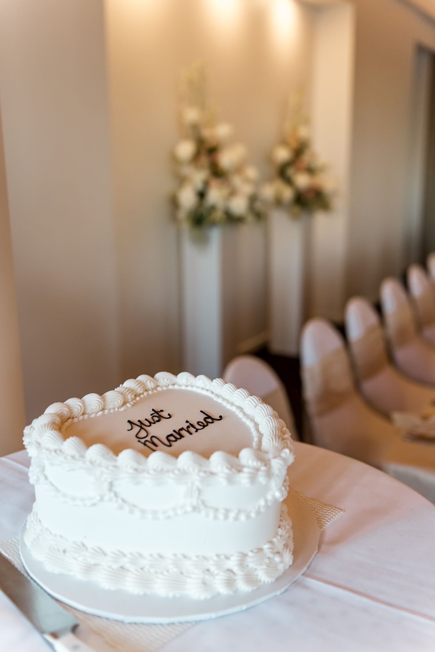 Heart-shaped white wedding cake inscribed with Just Married displayed in a decorated wedding reception hall.