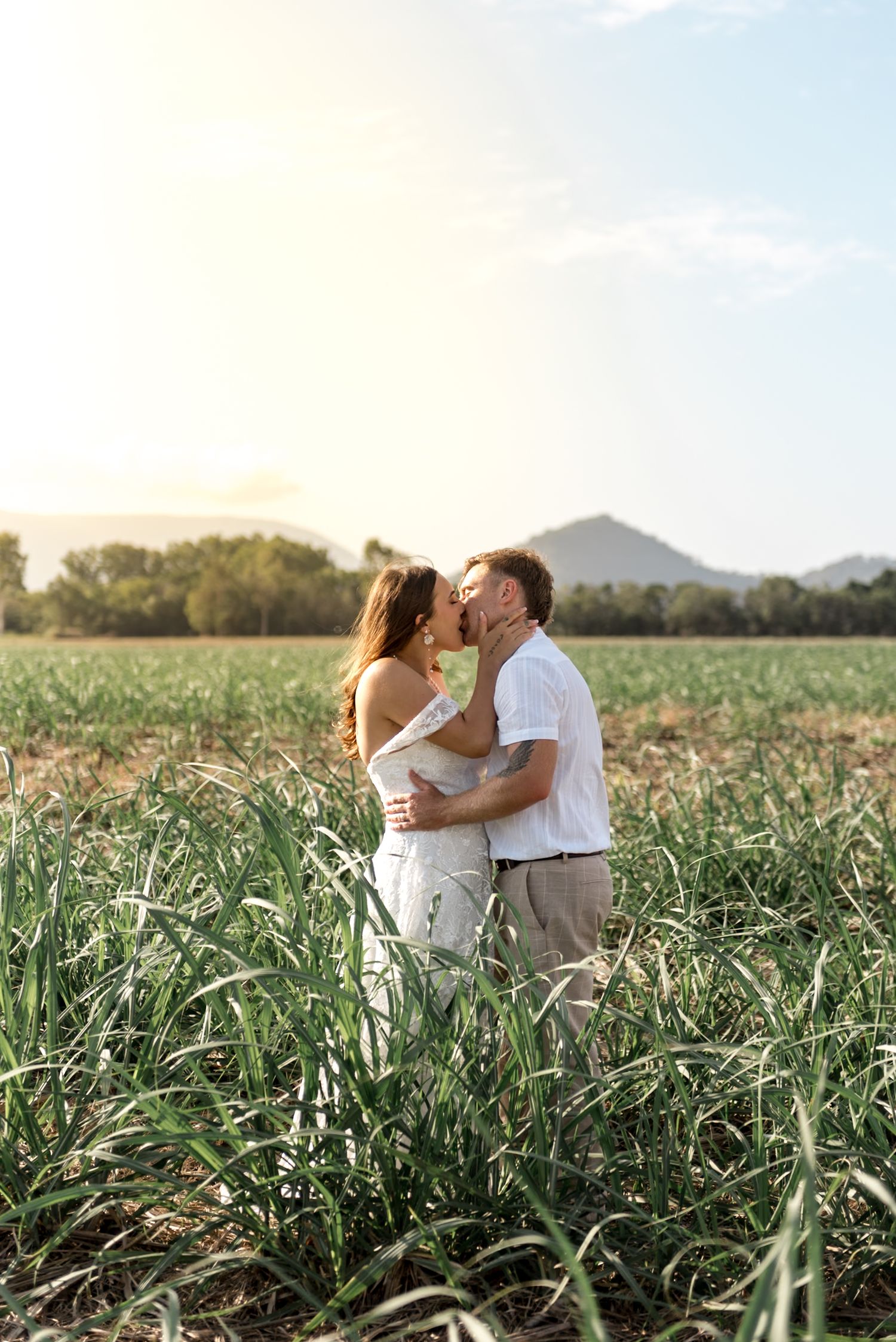 Couple sharing a kiss in a bright green field with mountains visible in the background.