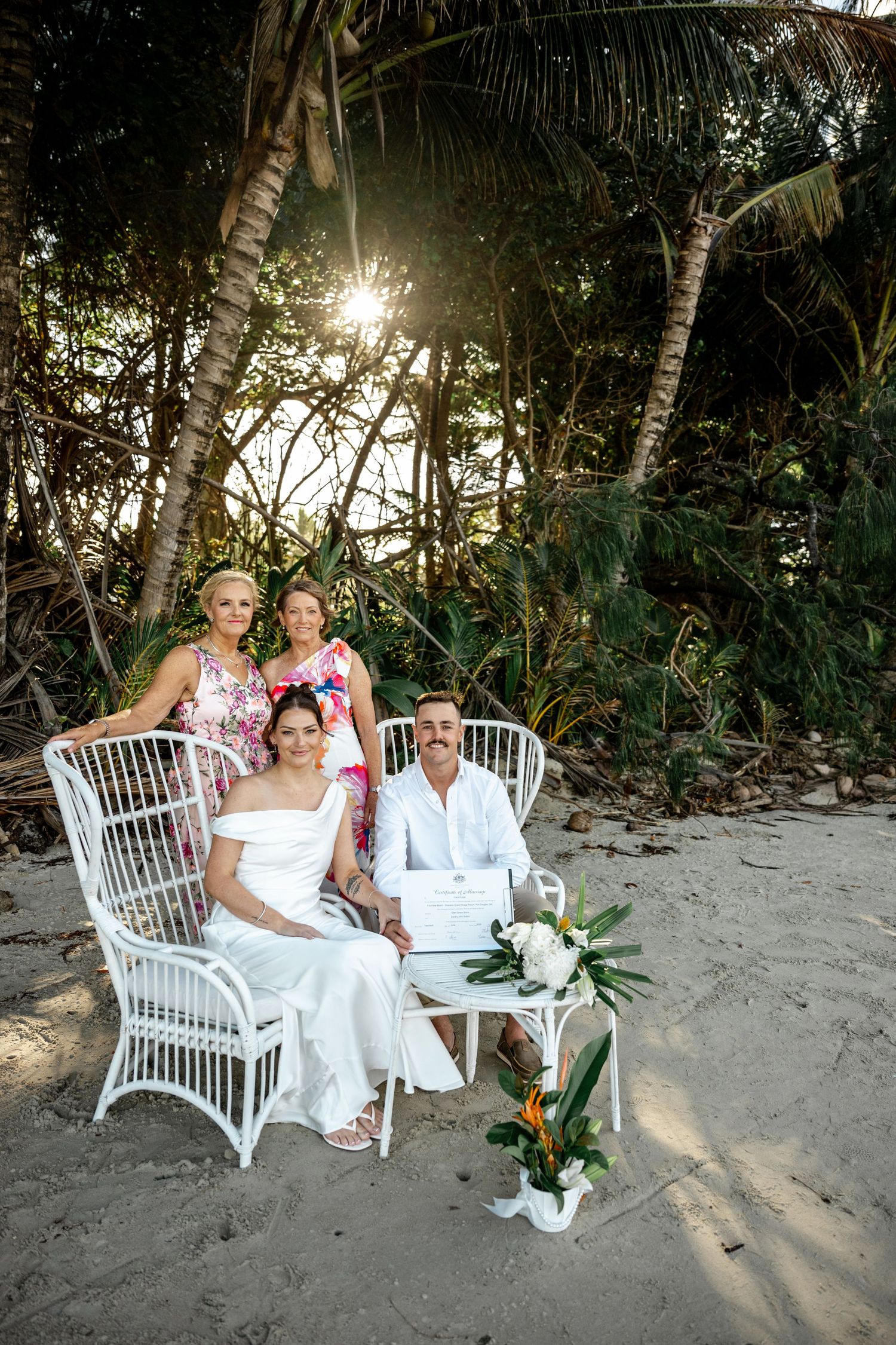Wedding couple seated with two guests on white rattan chairs on tropical beach at Four Mile Beach, Port Douglas.