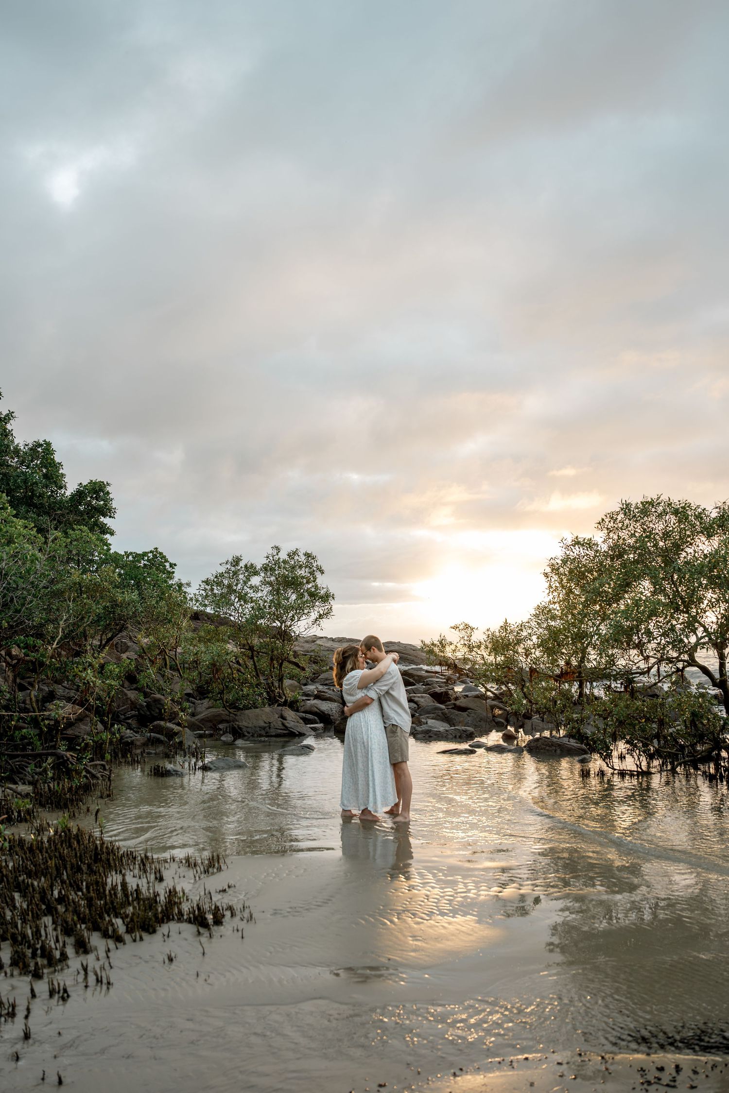 Couple embracing romantically in shallow water at sunset on a tropical beach with mangroves at Four Mile Beach, Port Douglas.