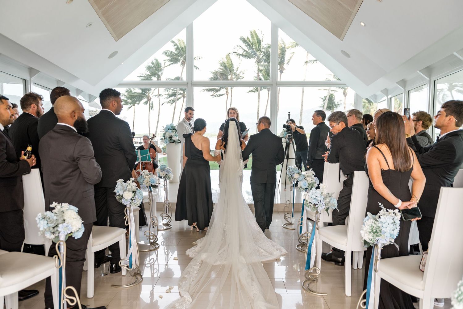 Wedding ceremony wide shot showing bride and groom at altar in glass chapel.
