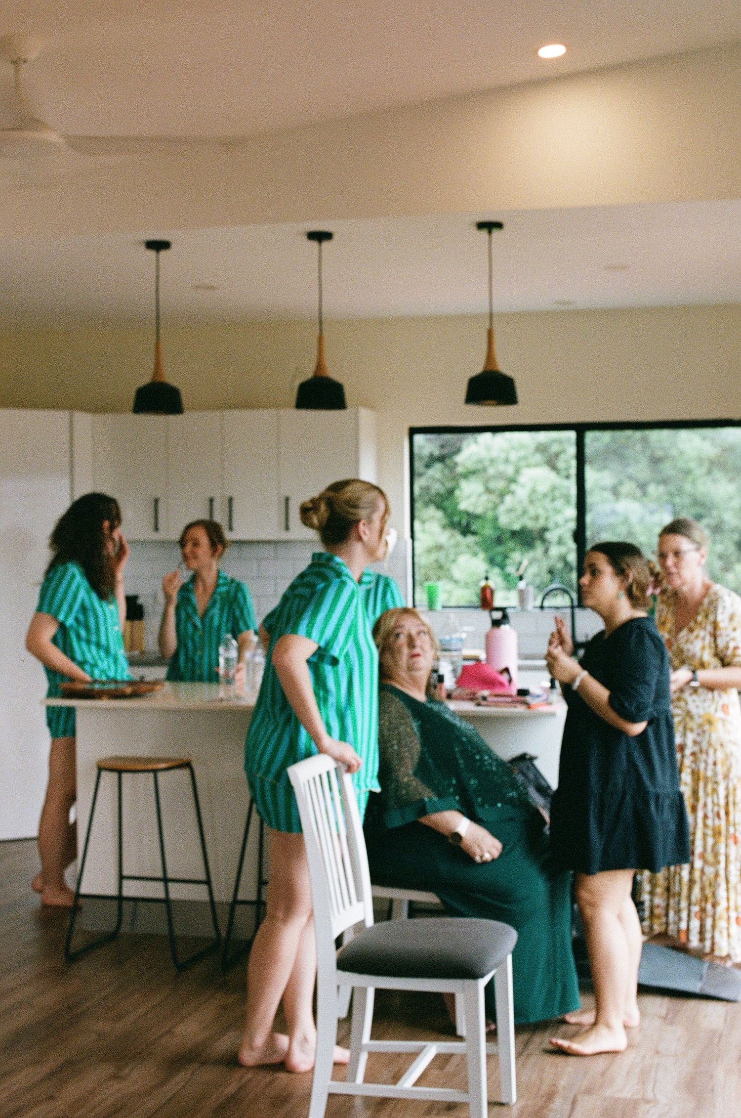 Bridesmaids in matching green striped pajamas gather in a modern kitchen during wedding preparations.