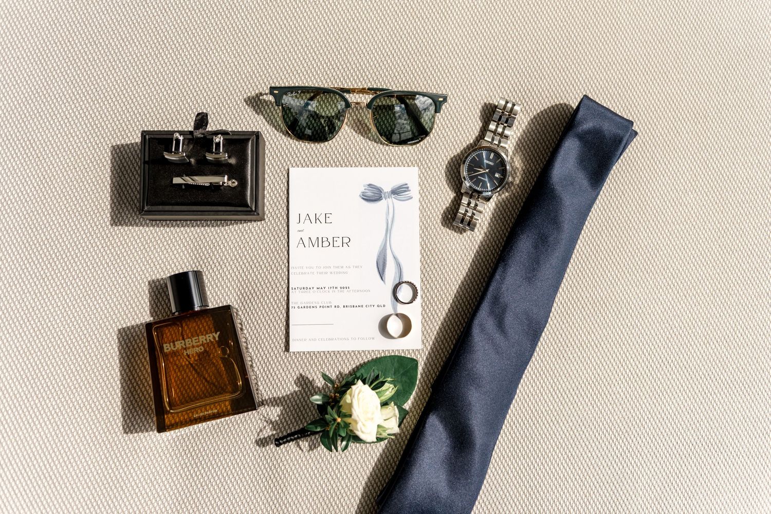 Groom wedding flat lay with invitation, navy tie, watch, sunglasses and cologne.