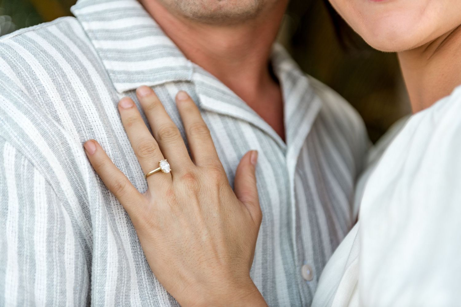 Close-up of womans hand with diamond engagement ring resting on mans striped shirt.