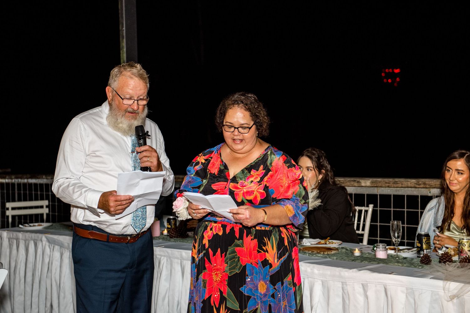 Older couple delivers heartfelt wedding speech together at elegant evening reception dinner.