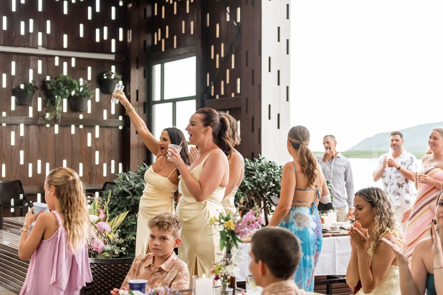 Bridesmaid giving a champagne toast speech at a warmly lit tropical wedding reception venue.