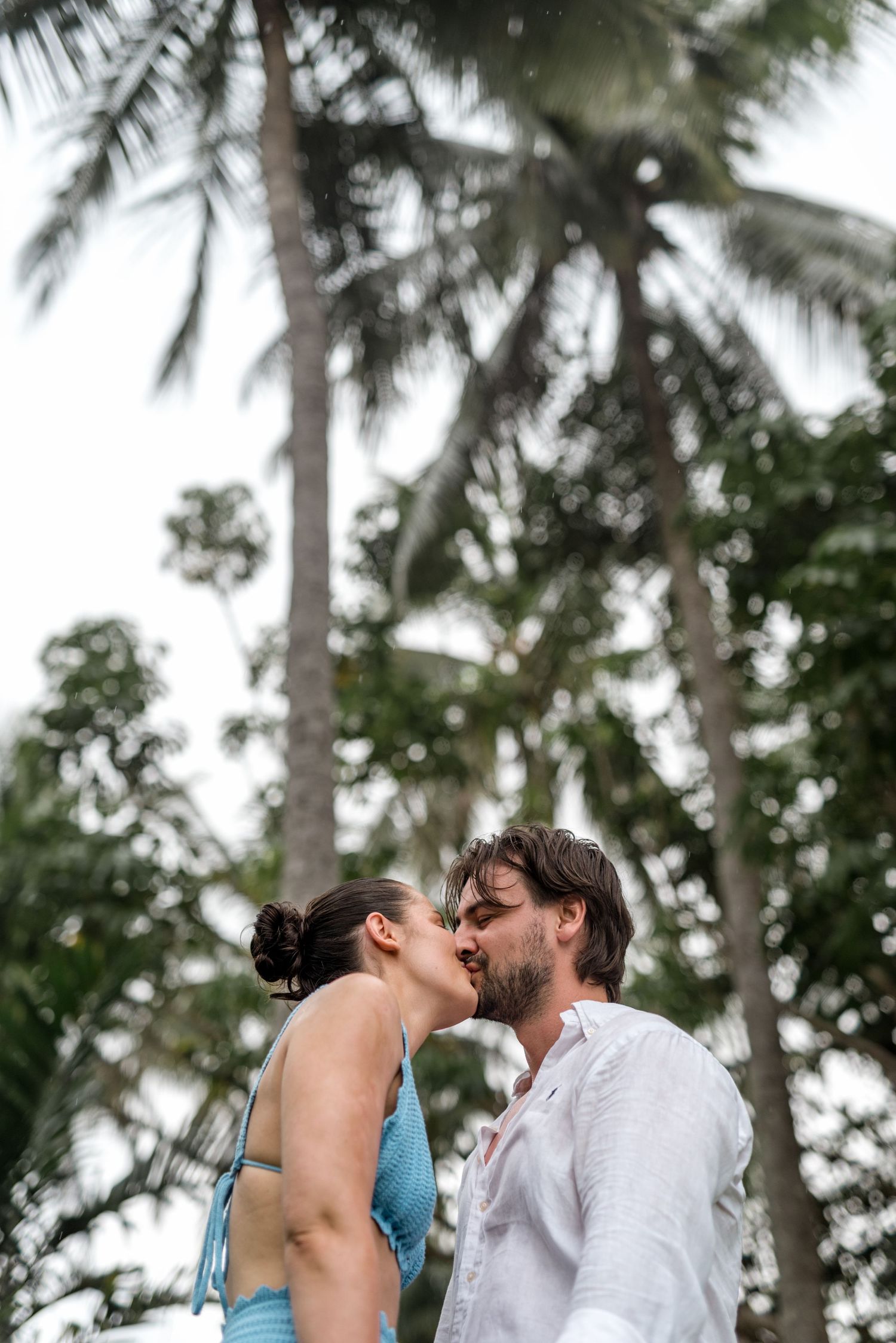 Couple sharing a kiss outdoors with tall tropical palm trees in the background.