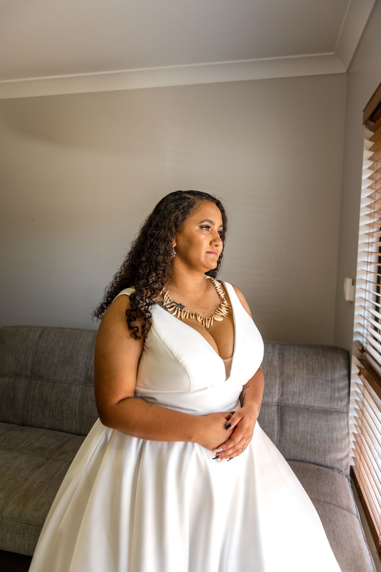 Bride in white V-neck wedding gown wearing gold statement necklace indoors.