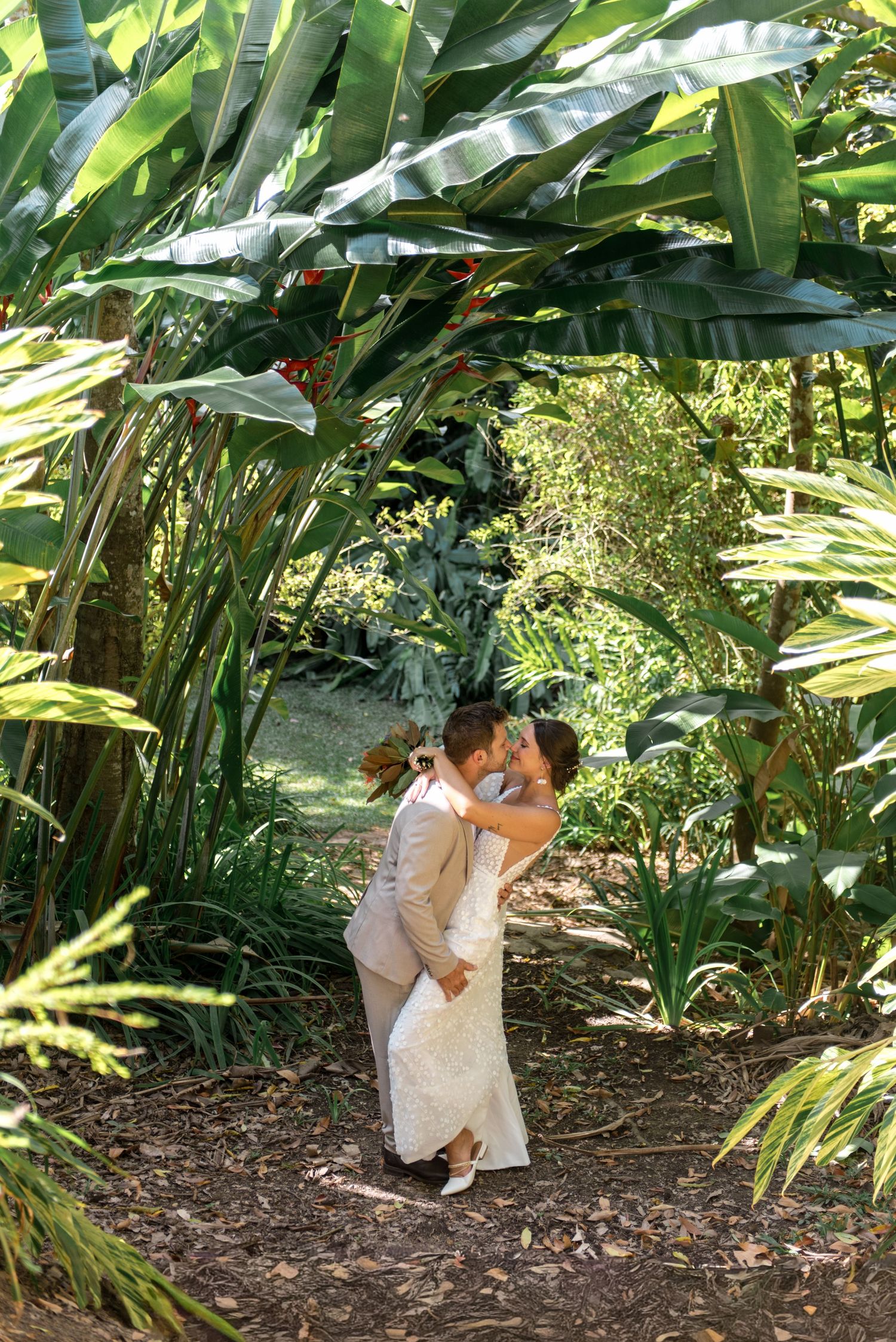 Bride and groom sharing a romantic kiss under an archway of tropical bird of paradise plants.
