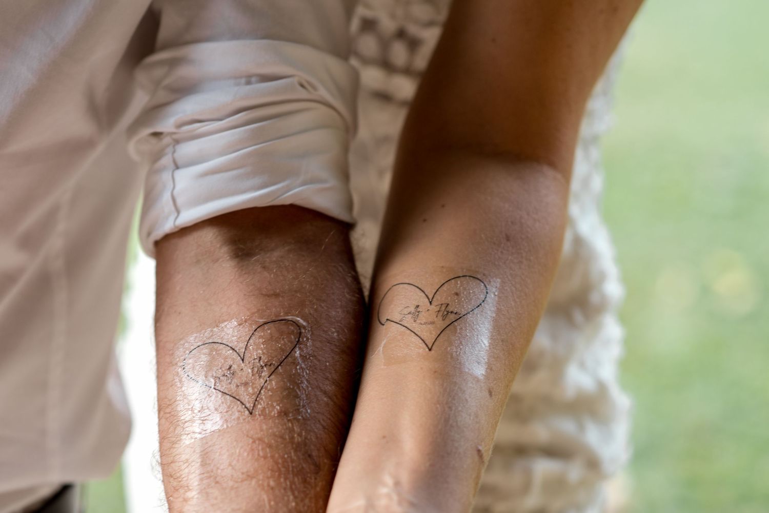 Close-up of couple showing matching heart tattoos on their forearms at wedding.