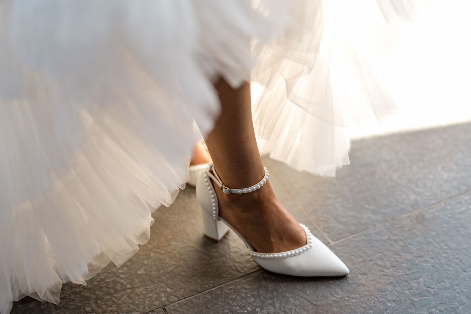 Bride wearing elegant white pearl-embellished block heel wedding shoes with ruffled gown.