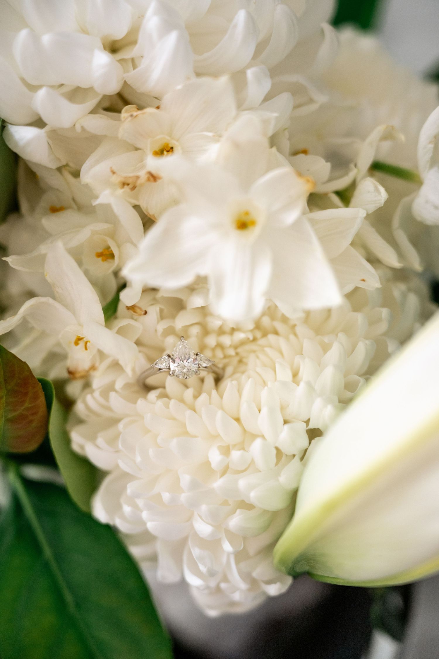 Diamond engagement ring nestled among white hyacinth and chrysanthemum blooms in a bridal bouquet.