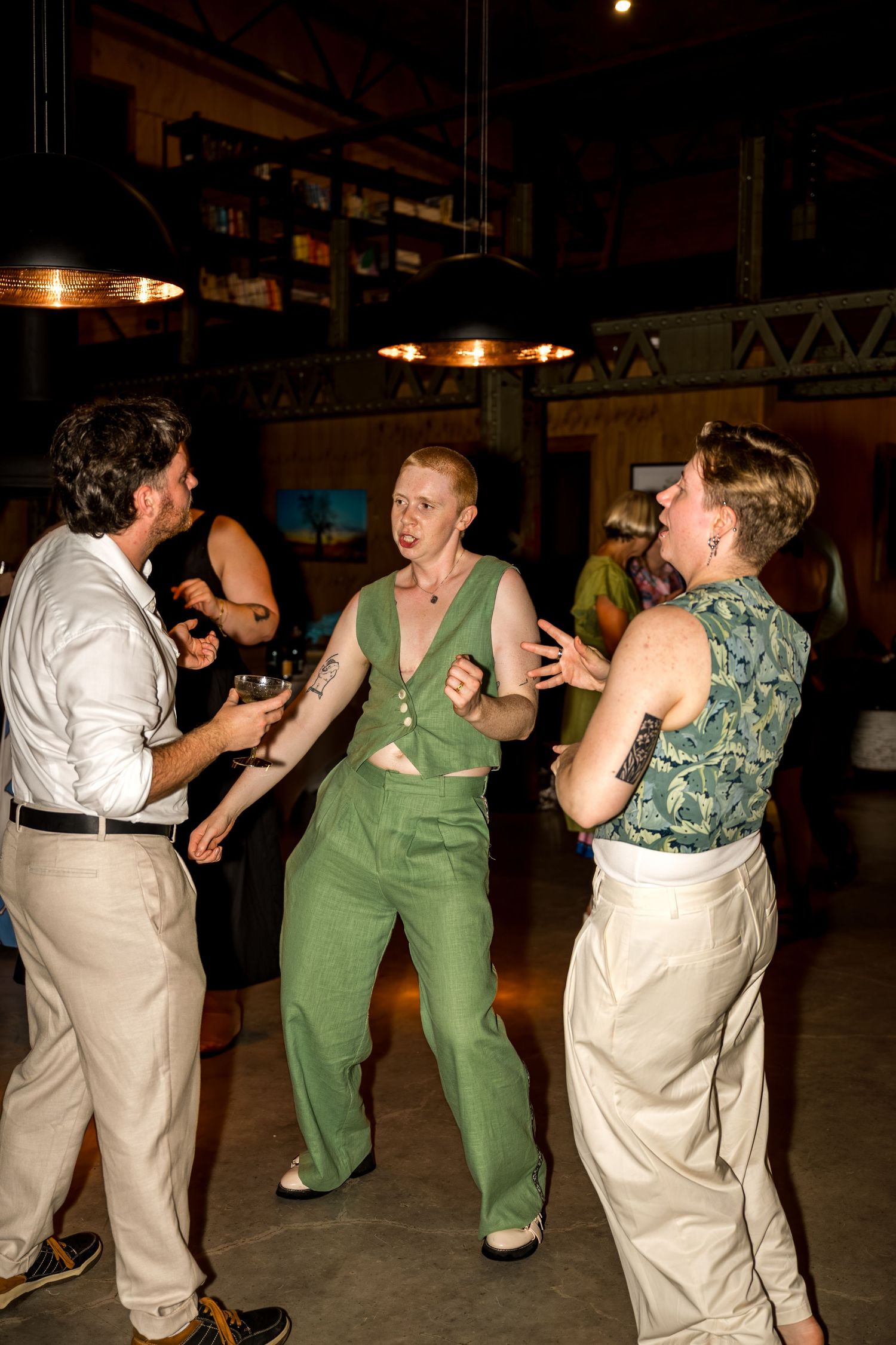 Three guests dancing energetically at an indoor wedding reception in a rustic venue.