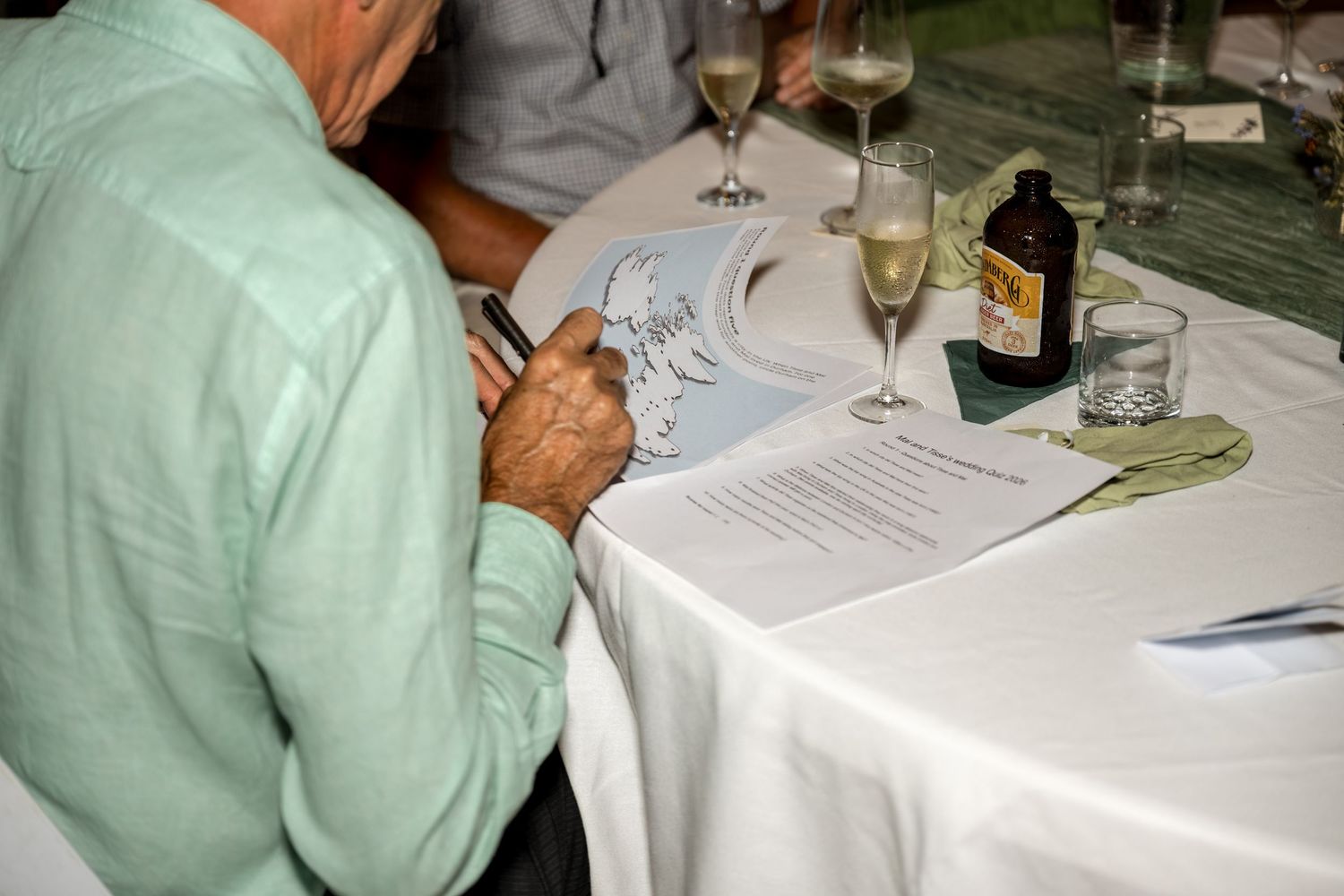 Guest reviewing a menu or document at a formal dinner table with wine glasses and bottles.