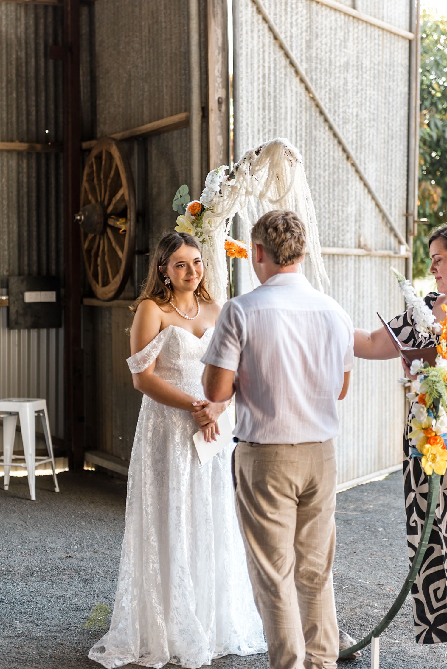 Bride in lace gown and groom exchange vows in rustic barn wedding venue.