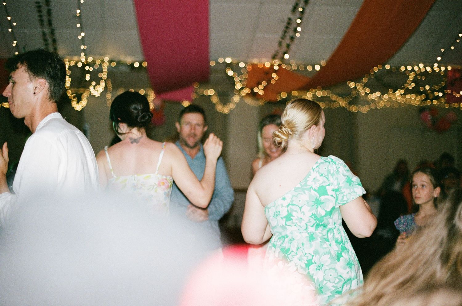 Guests dance joyfully on a decorated wedding reception dance floor with festive lighting.