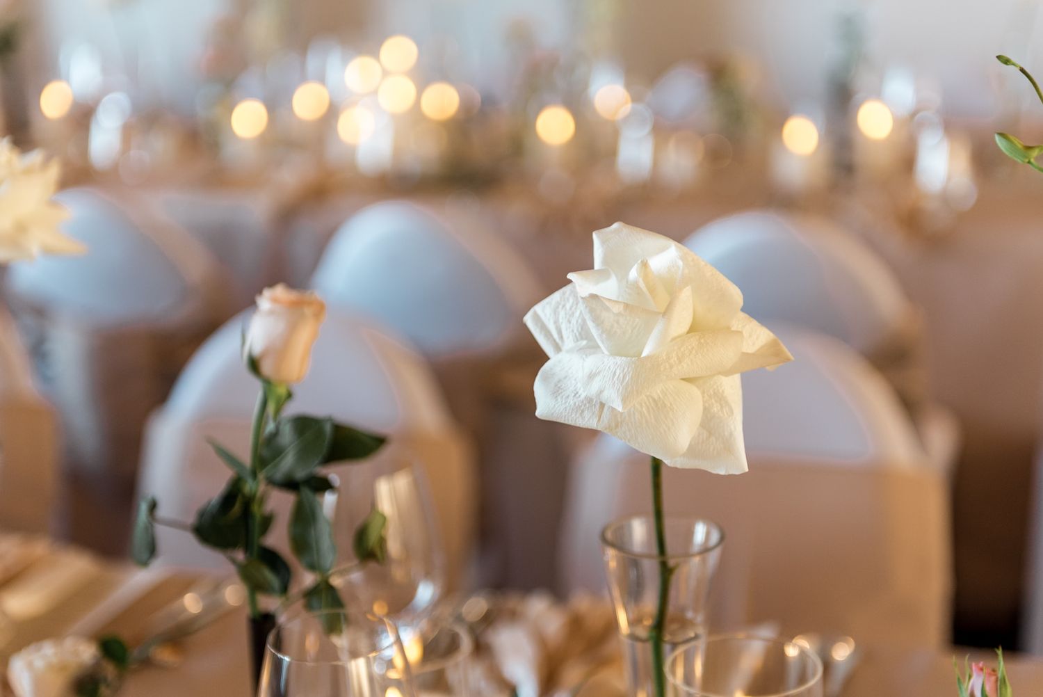 White rose in glass vase centerpiece with blush roses and candlelight at an elegant wedding reception.