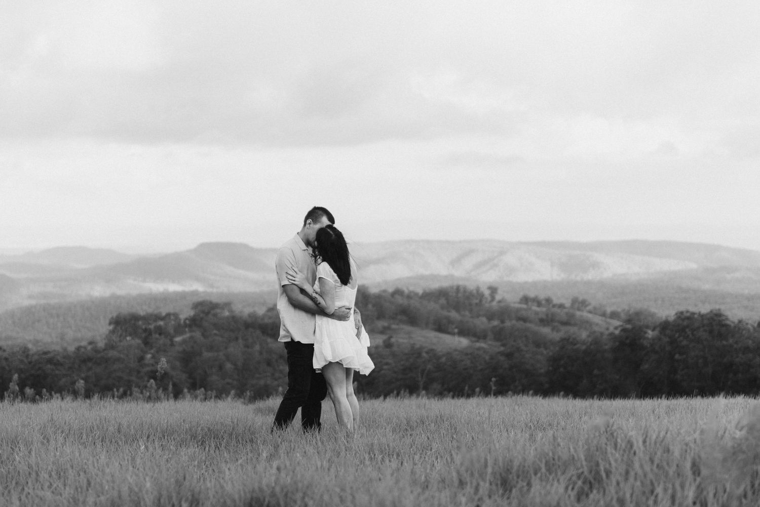 Black and white romantic couple kissing in an open field with mountain landscape.