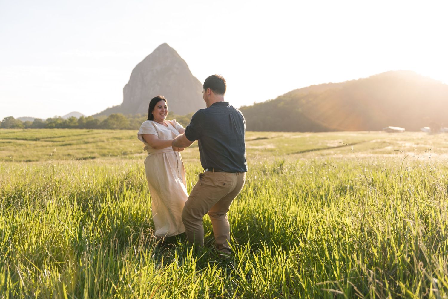 Couple dancing playfully in a green field with a large rocky mountain glowing in the sunset.