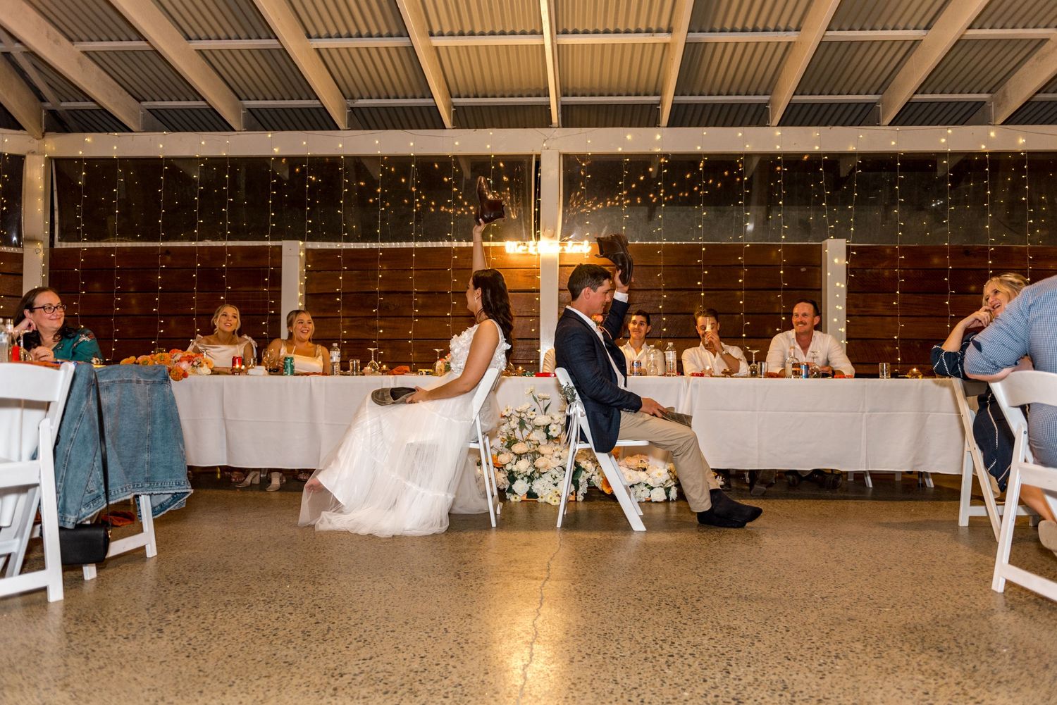 Bride and groom seated at head table during elegant fairy light wedding reception.