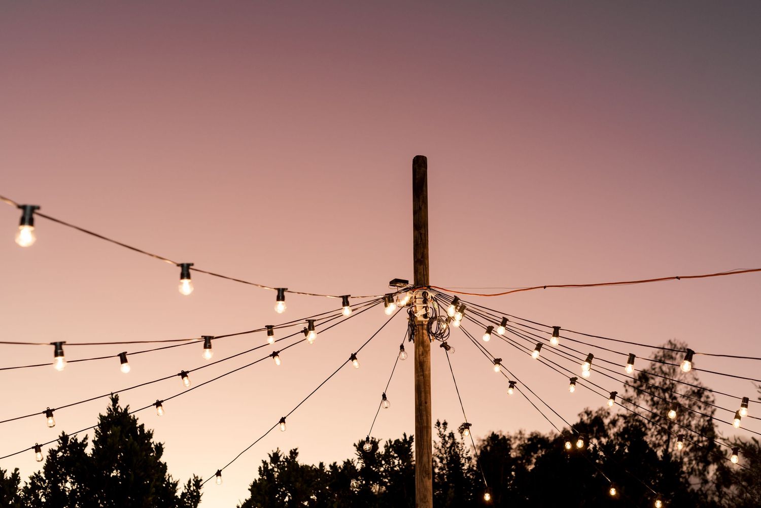 Decorative string lights radiating from a central pole against a pink sunset sky.