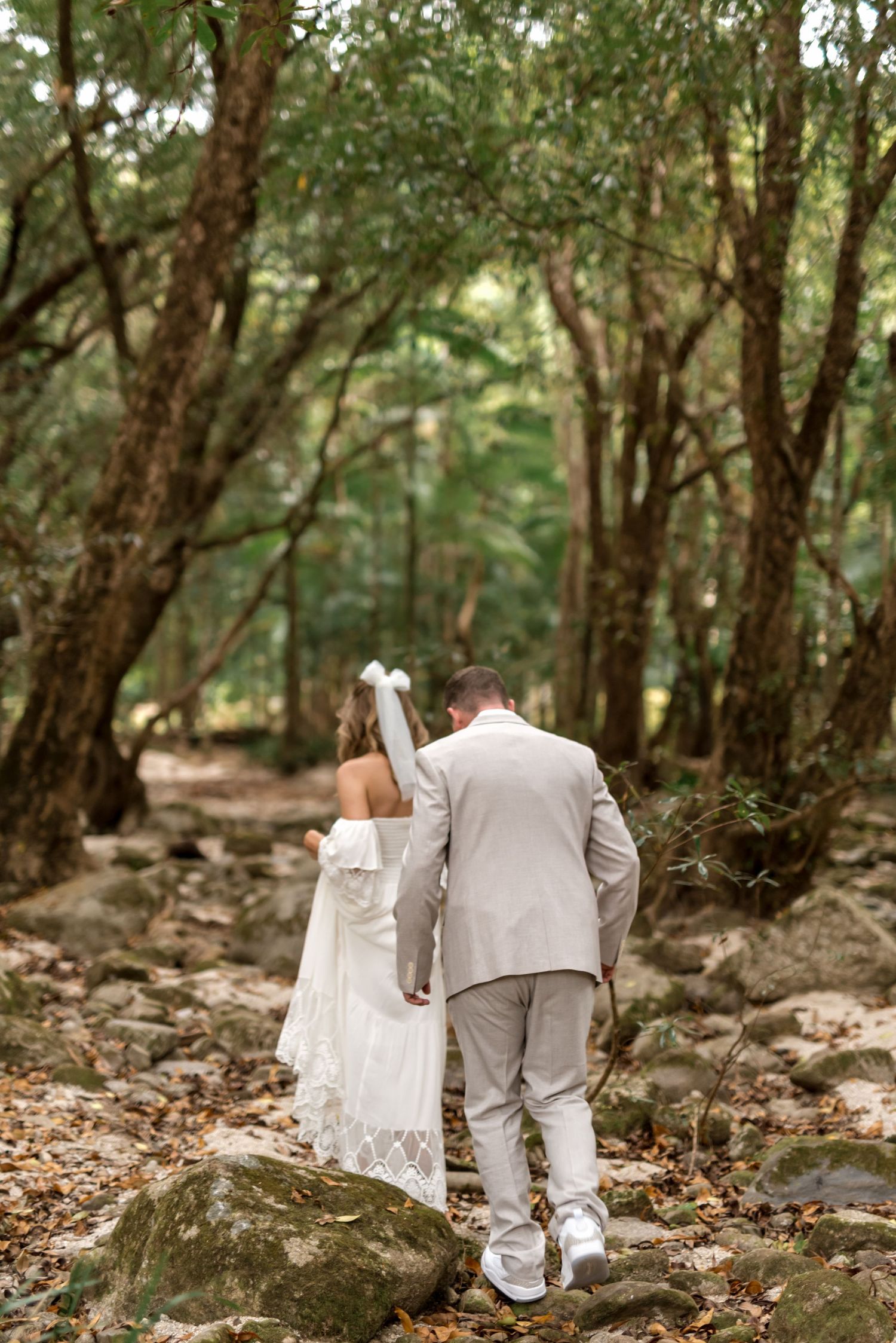 Bride and groom walking hand in hand along a rocky forest path after wedding.