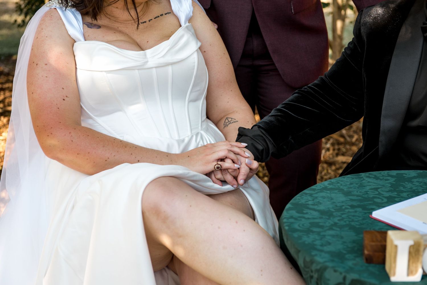 Bride and groom hold hands at signing table during outdoor wedding ceremony.