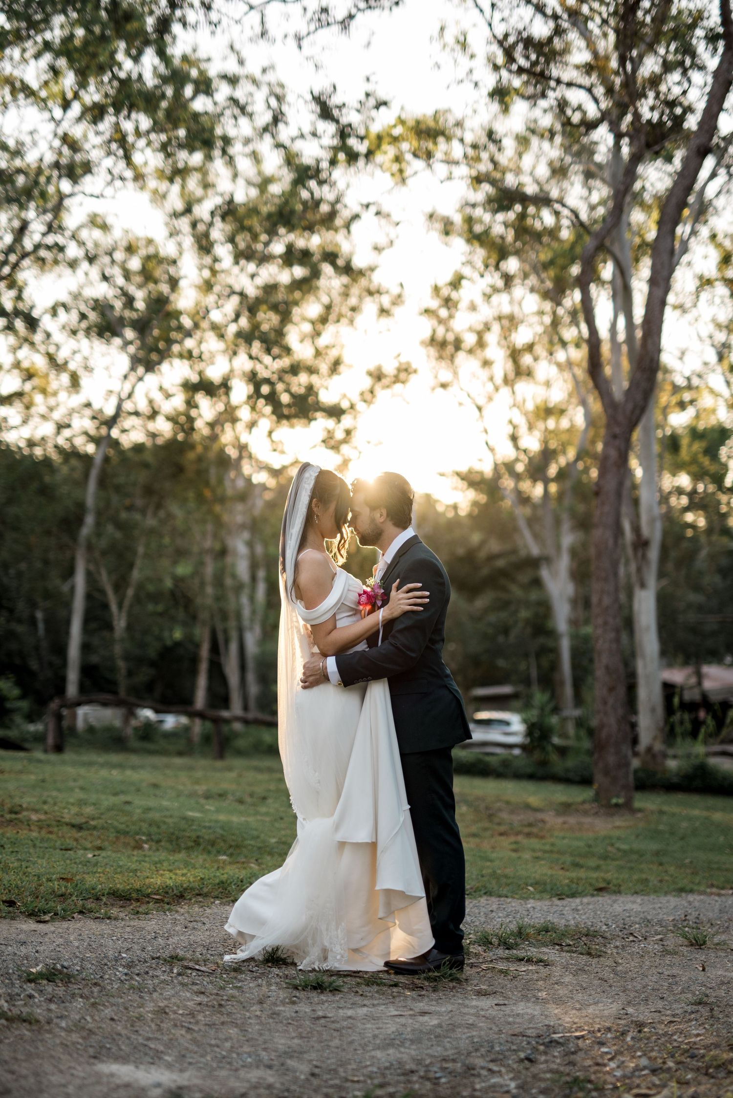 Bride and groom share a tender moment at golden hour in a forest setting.