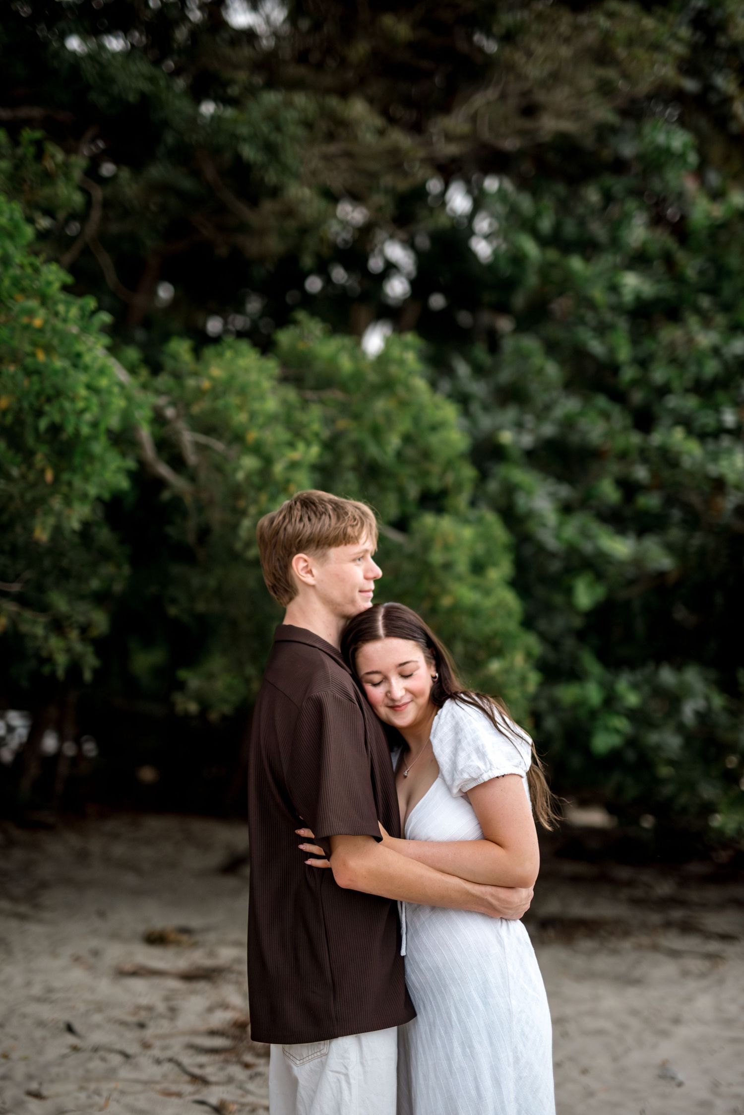 Young man holding woman close as she rests her head on his chest on a tropical beach.