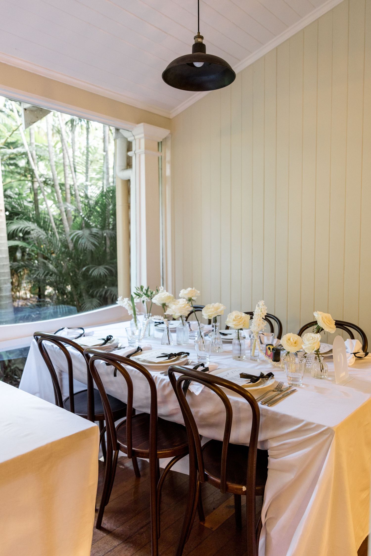 Intimate wedding dining room with long table, bentwood chairs, and white rose centerpieces.