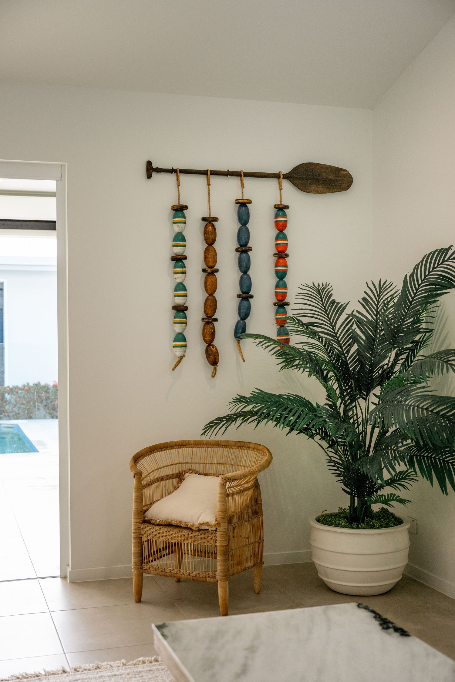 Bohemian interior with rattan chair, tropical palm plant, and colorful beaded wall art decoration.