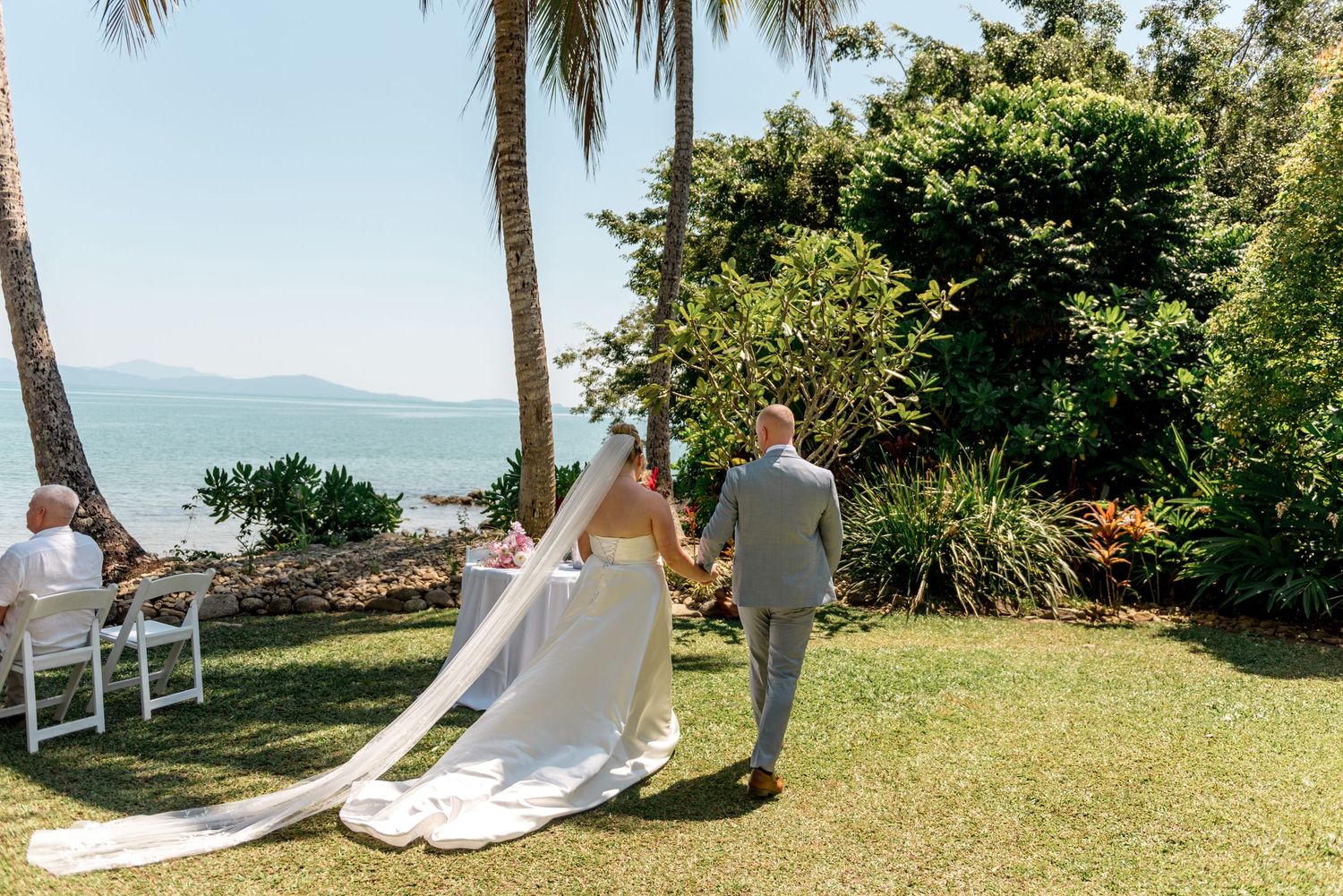 Bride and groom walking through tropical garden after beach wedding.